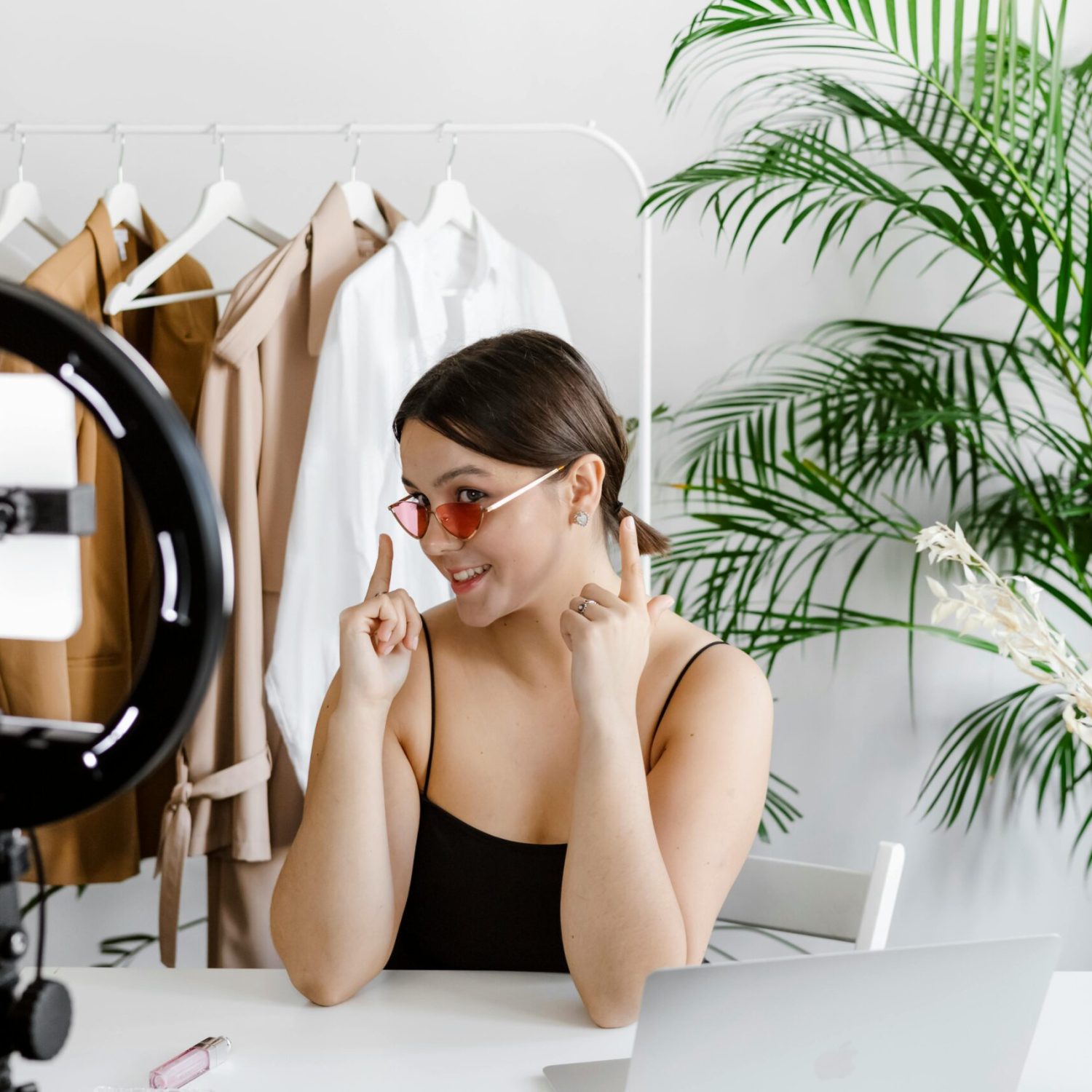 Stylish woman vlogging with ring light, surrounded by fashion accessories and greenery.