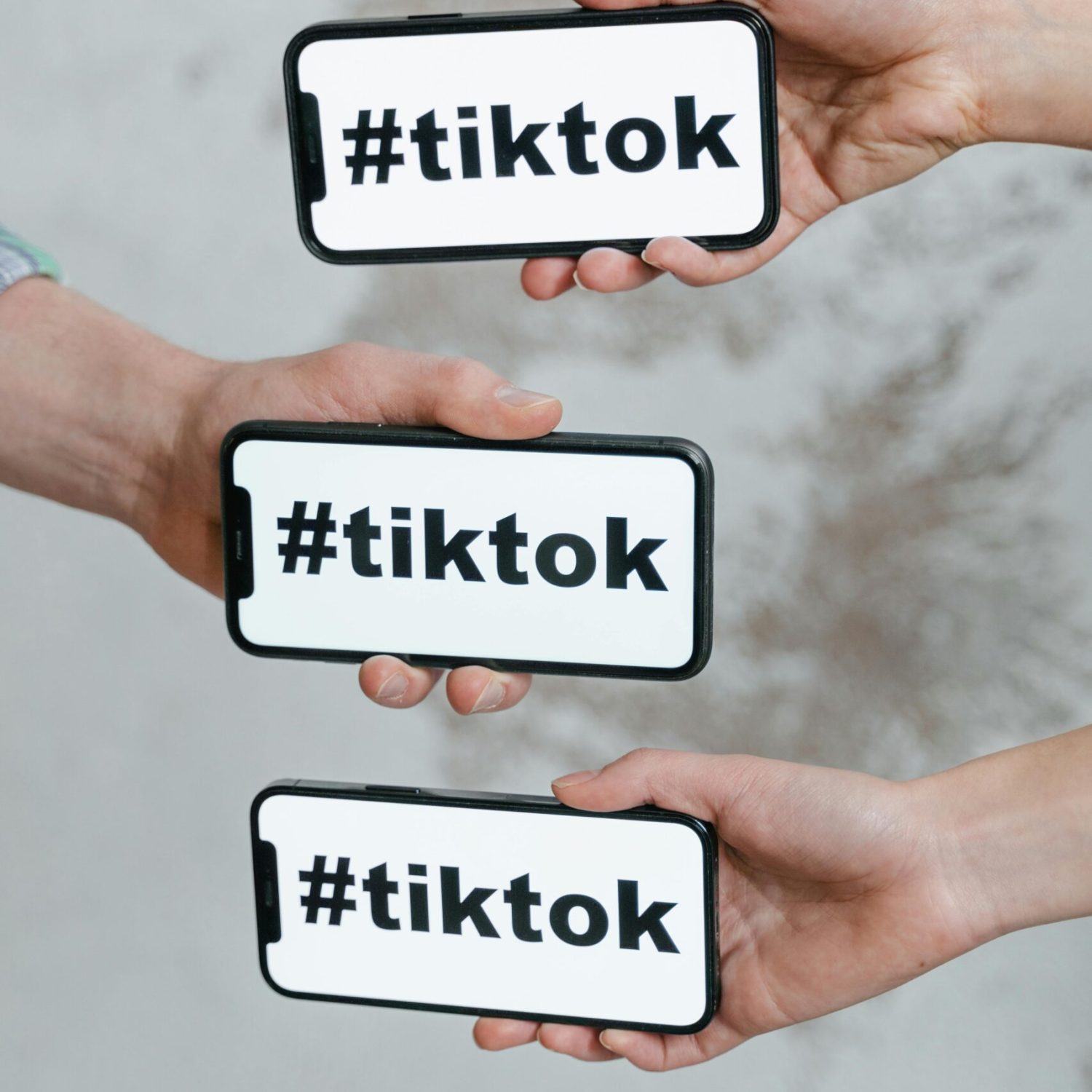 Hands holding smartphones displaying TikTok hashtag, emphasizing social media connection.