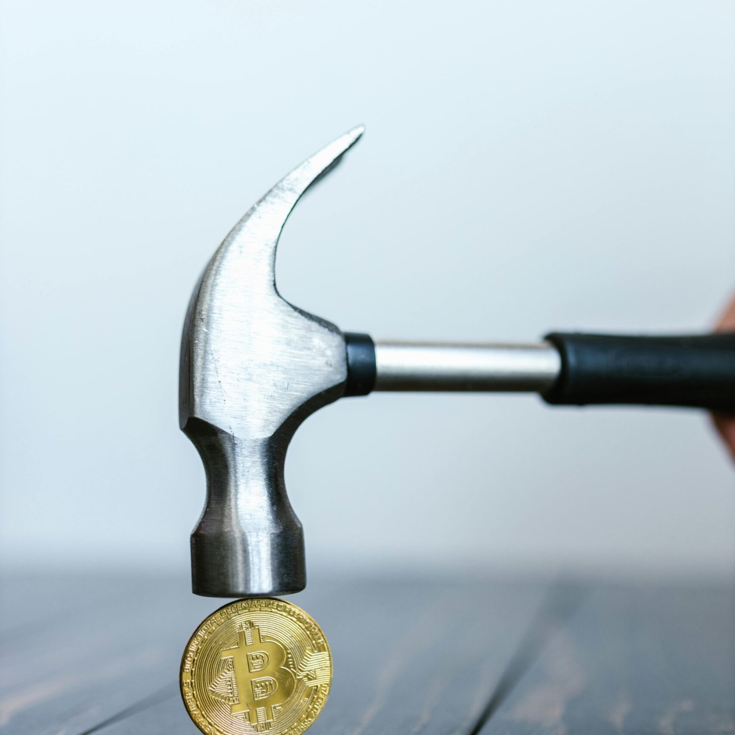 Close-up of a hammer striking a Bitcoin coin on a wooden surface, symbolizing cryptocurrency impact.